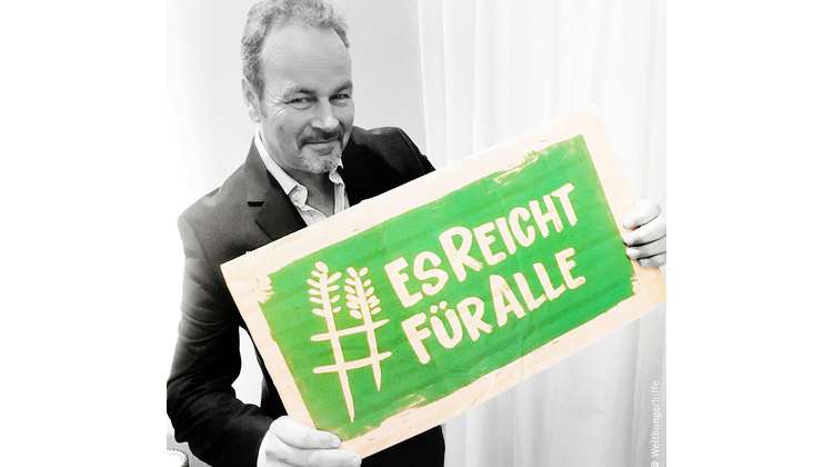 Schauspieler Till Demtrøder hält ein Schild mit dem Welthungerhilfe-Hashtag #EsReichtFürAlle.
