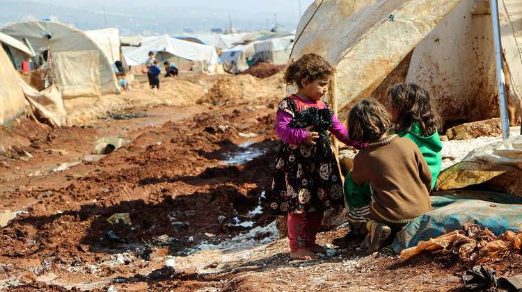 Drei Kinder hocken auf dem schlammigen Boden in einem Camp für Binnenflüchtlinge in Nord-Aleppo, Syrien. 