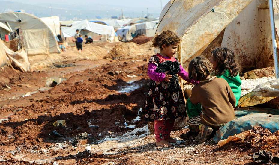 Drei Kinder hocken auf dem schlammigen Boden in einem Camp für Binnenflüchtlinge in Nord-Aleppo, Syrien. 