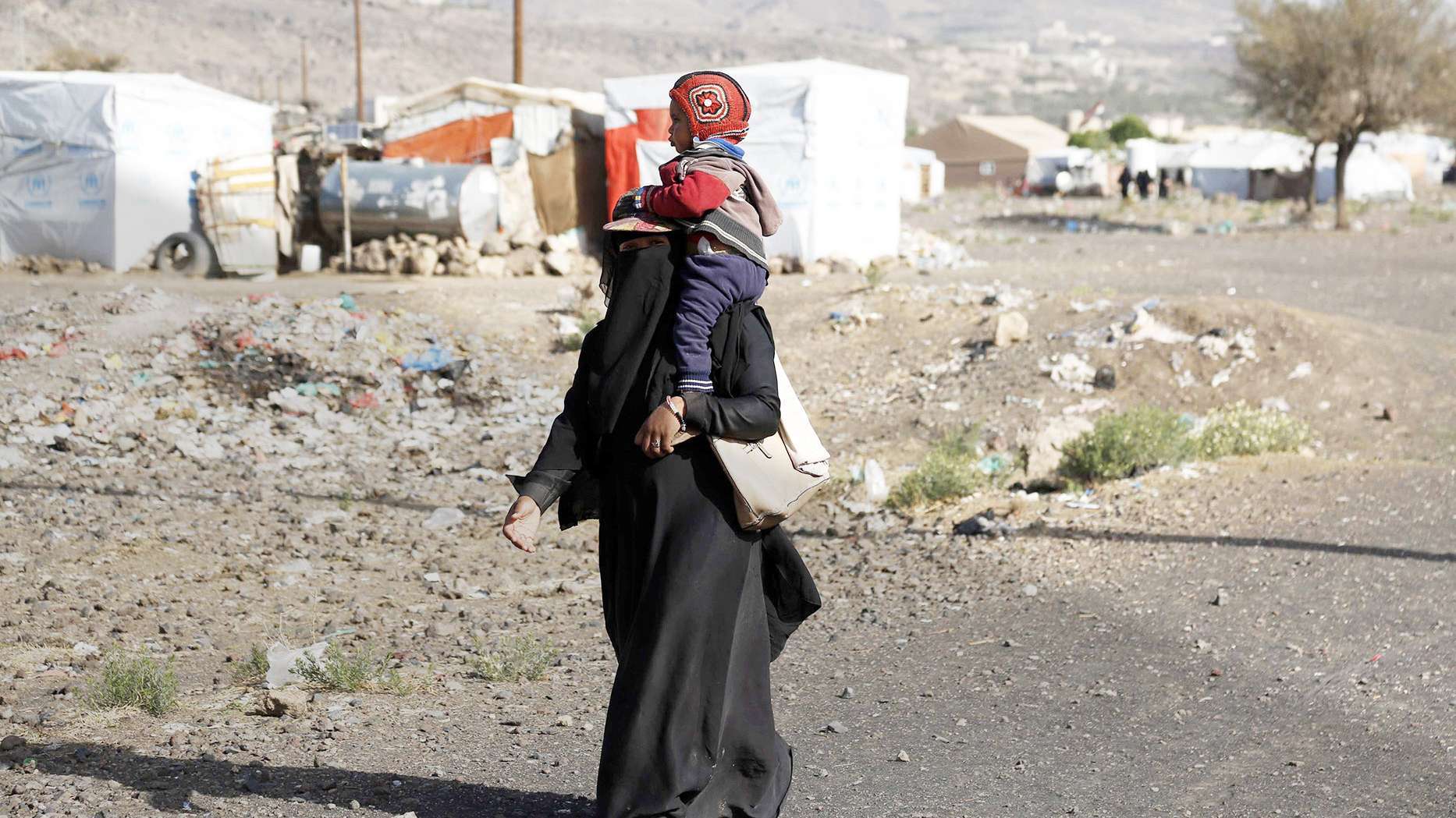 Eine Mutter trägt ihr Kind durch das Dharawan Flüchtlingscamp in Sanaa, Jemen. Die Menschen im Camp kämpfen unter schwierigen Bedingungen ums Überleben. 