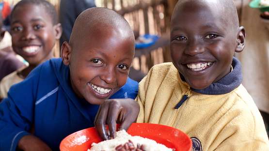 Zwei Kinder essen Bohnen und Reis aus einem Teller und lächeln